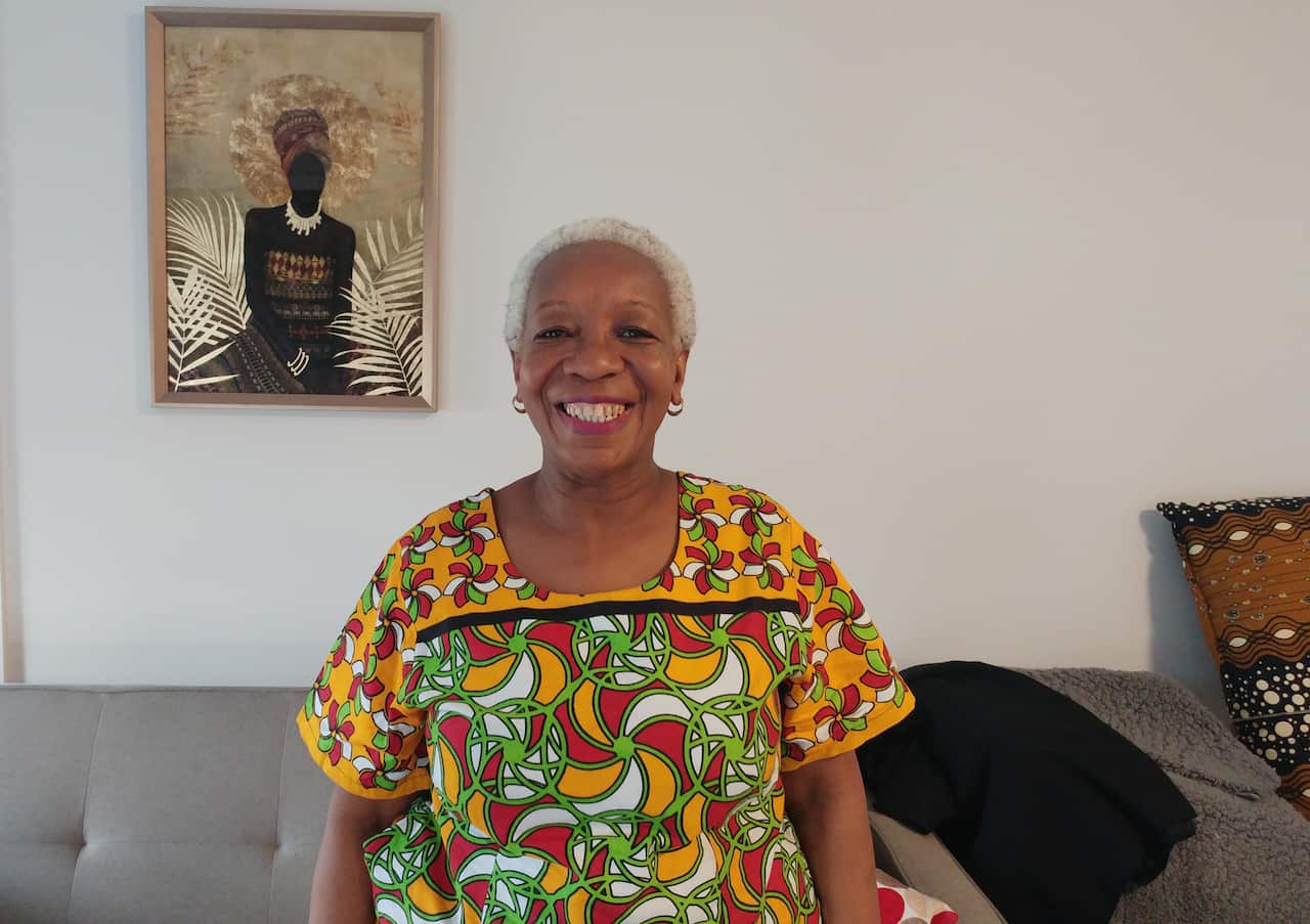 Joy dressed in bright kenyan printed top standing in front of wall featuring picture with man dressed in traditonal Kenyan attire