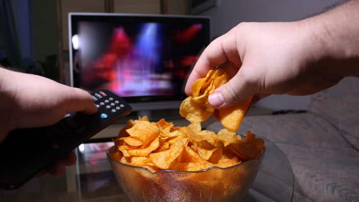 Person changing the TV station and reaching for potato chips