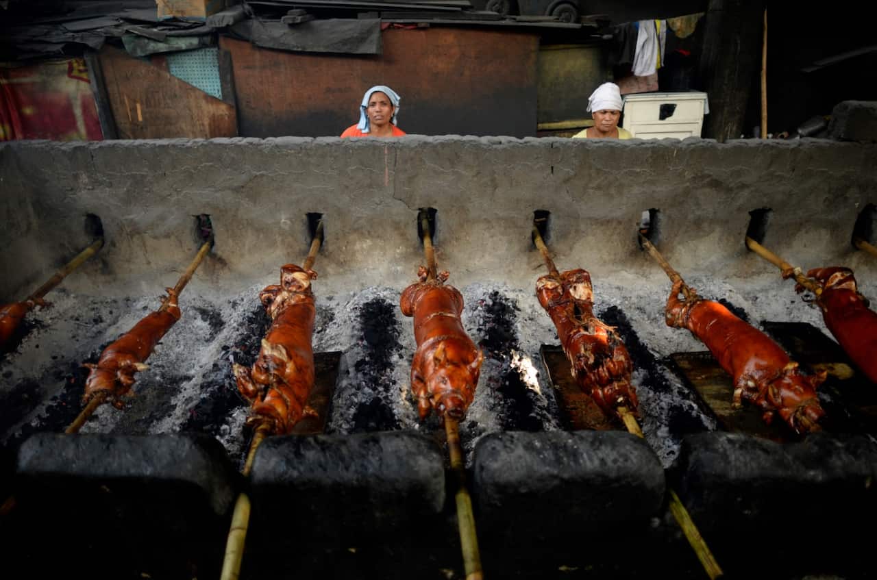 Workers rotate bamboo skewered pigs, or Lenchon, as they are roasted over hot coals in Manila