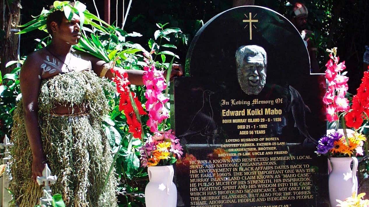 A woman in traditional dress stands next to Koiki Mabo's grave on Mer Island in the Torres Strait.