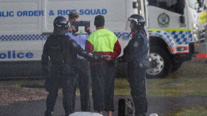 Riot police lead a detainee away in handcuffs during a riot at the Frank Baxter Juvenile Justice Centre, Kariong, NSW