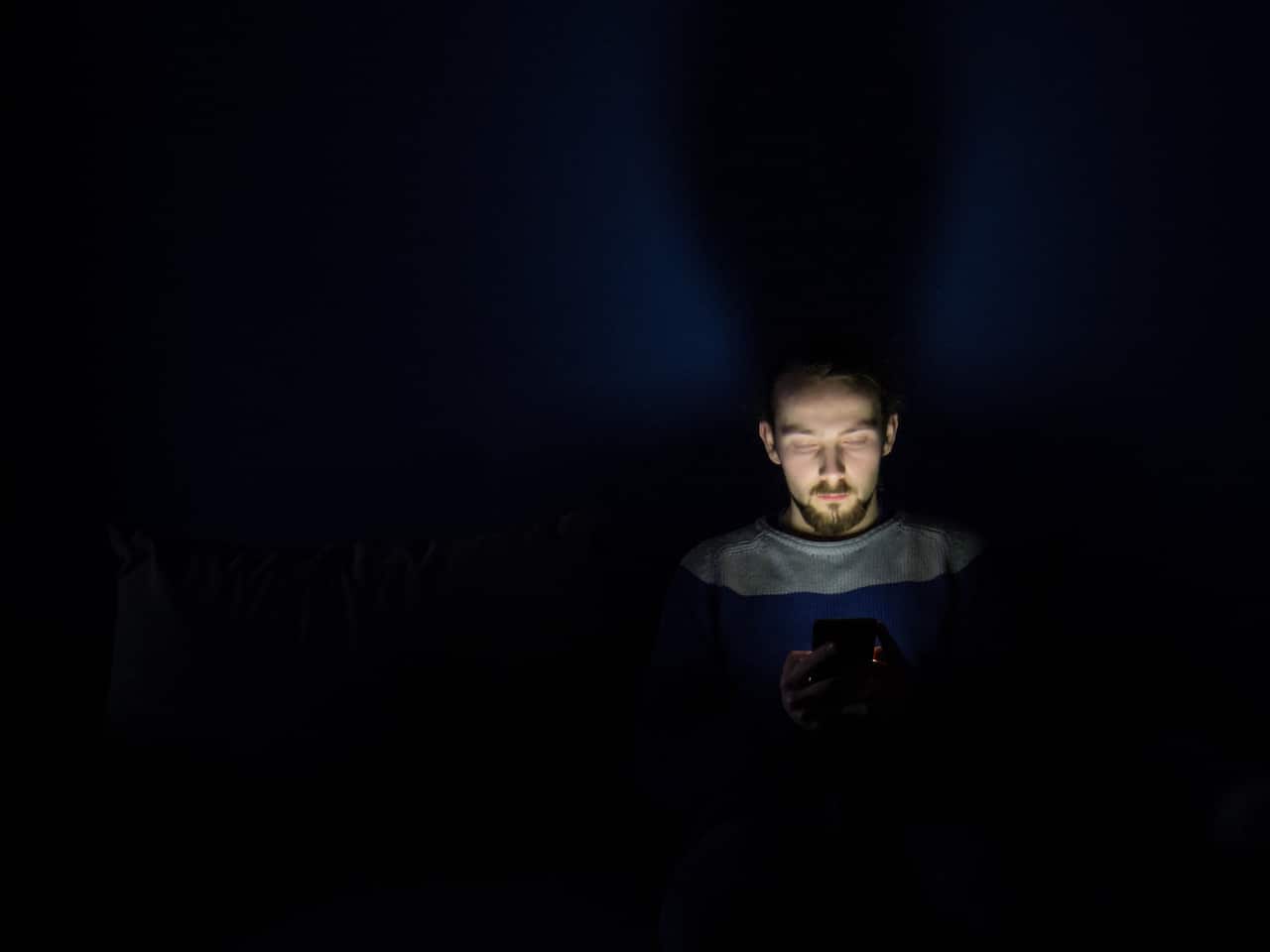 Image of a man using a mobile phone at night with visible blue light emitting from its screen.