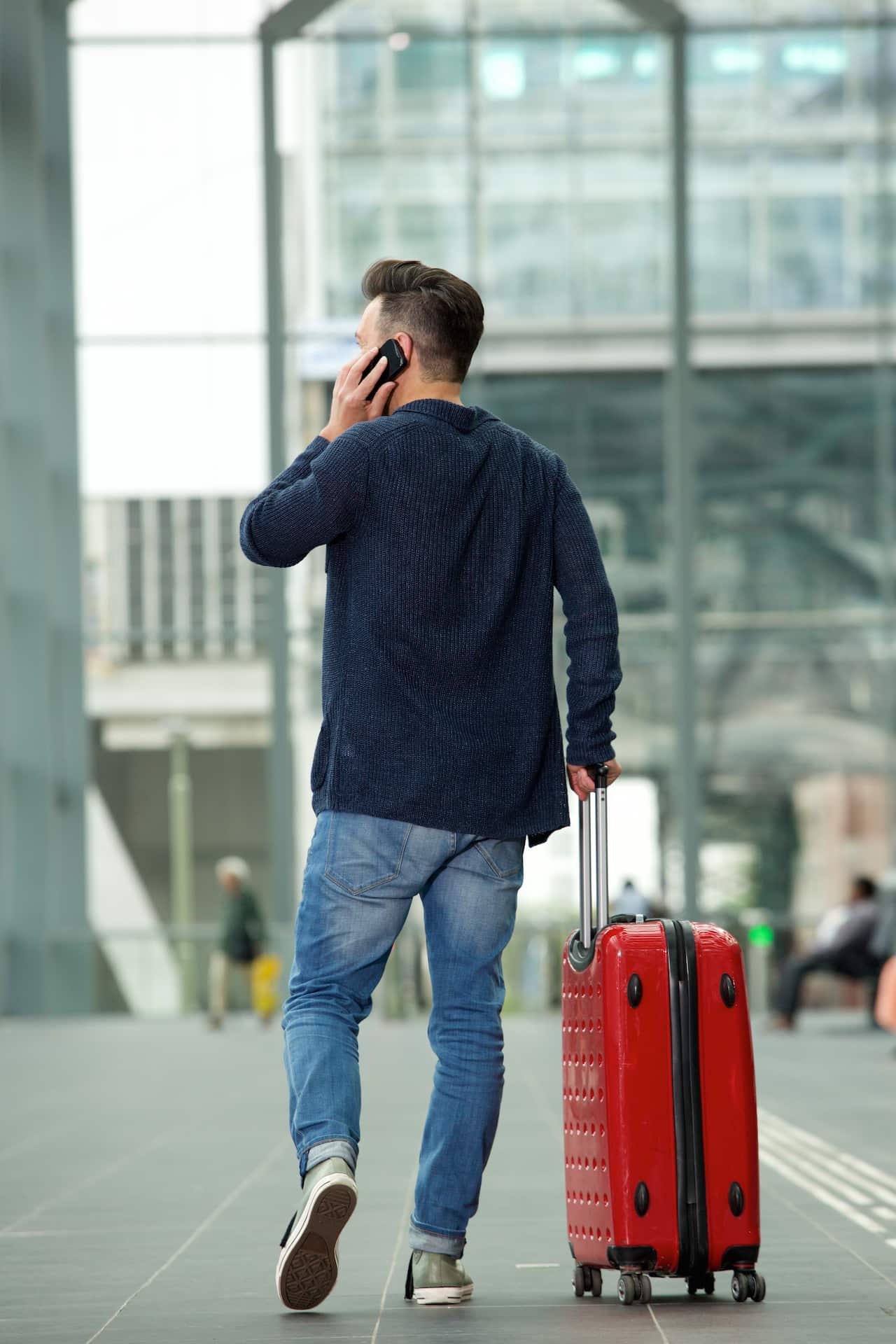 Rear view portrait of man walking in airport with travel bag and talking on mobile phone