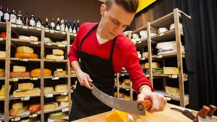 Male salesperson cutting cheese in store