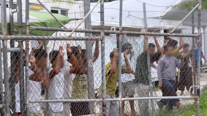 Asylum seekers staring at media from behind a fence at the Oscar compound in the Manus Island detention centre