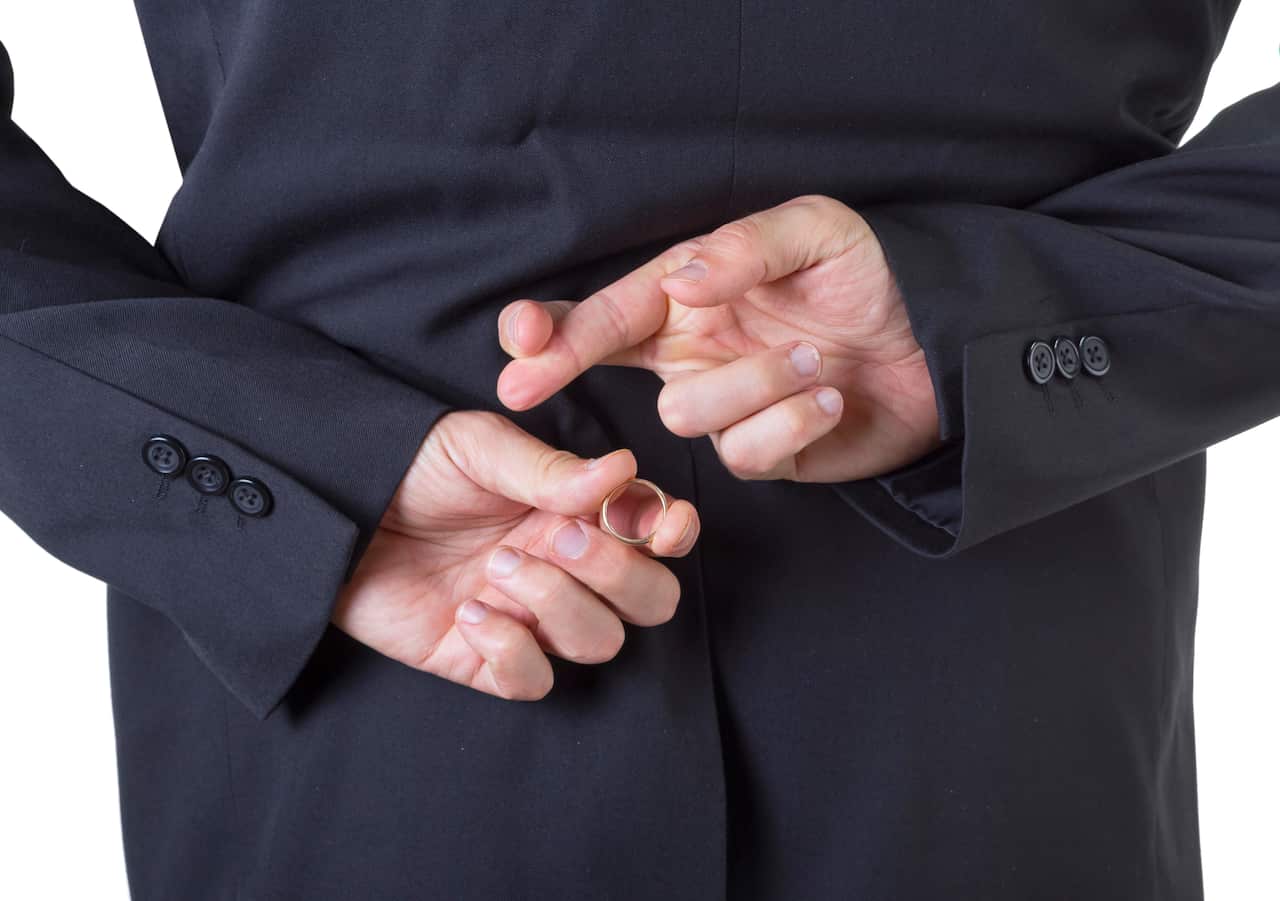 Man removing marriage ring from his finger behind his back isolated on white background.