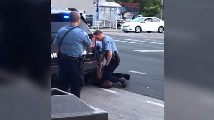 Người đàn ông da màu bị còng tay nằm úp mặt trên đường.