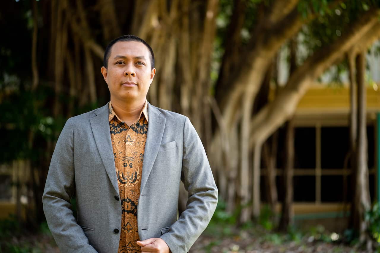 Mujiburrahman posing in the front of his office at Building Red 6, at the University of Charles Darwin
