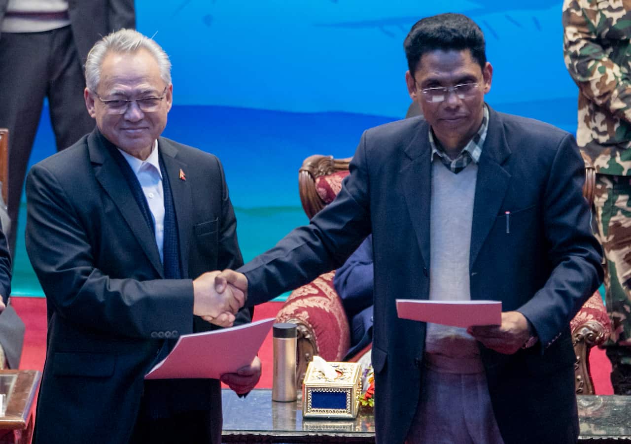 Nepal Home Minister Ram Bahadur Thapa, left, and the spokesperson of the Nepal Communist Party group Khadga Bahadur Bishwakarma shake hands during a signing of peace agreement in Kathmandu, Nepal, March 5, 2021. 
