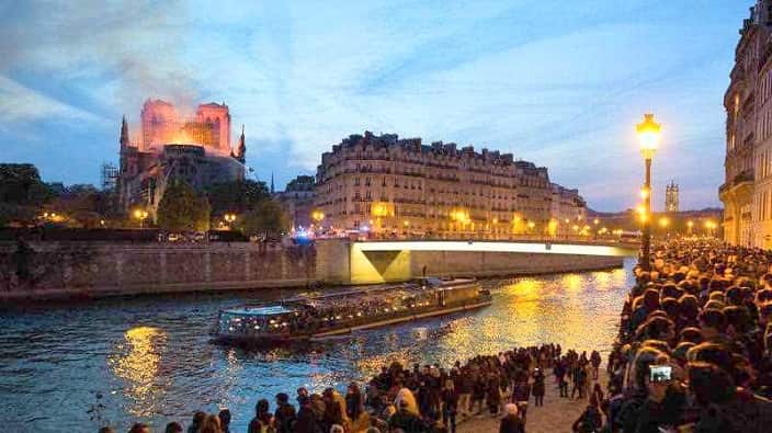 Bystanders look on as flames and smoke are seen billowing from the roof at Notre-Dame Cathedral.