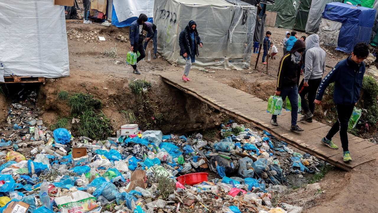 Moria camp detainees walking past pile of gargage