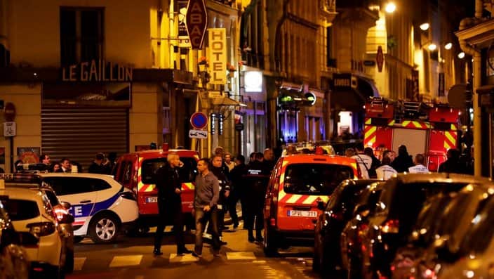 Policemen and emergency service members stand in a blocked street in Paris centre after one person was killed and several injured