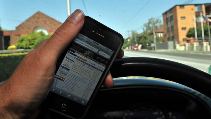 A driver holds a mobile phone whilst driving in Melbourne.
