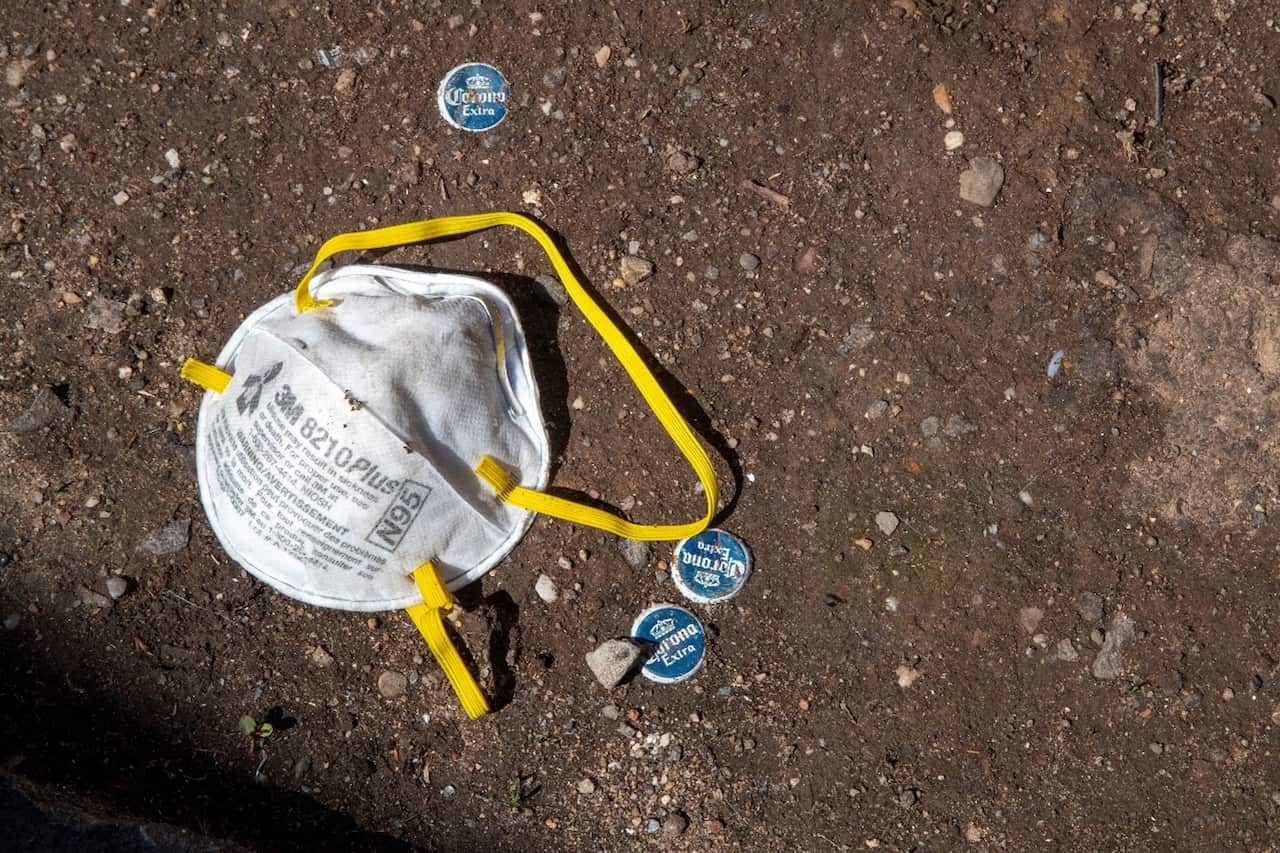 A N95 mask is seen on the sidewalk next to corona beer bottle caps outside a Medical Center