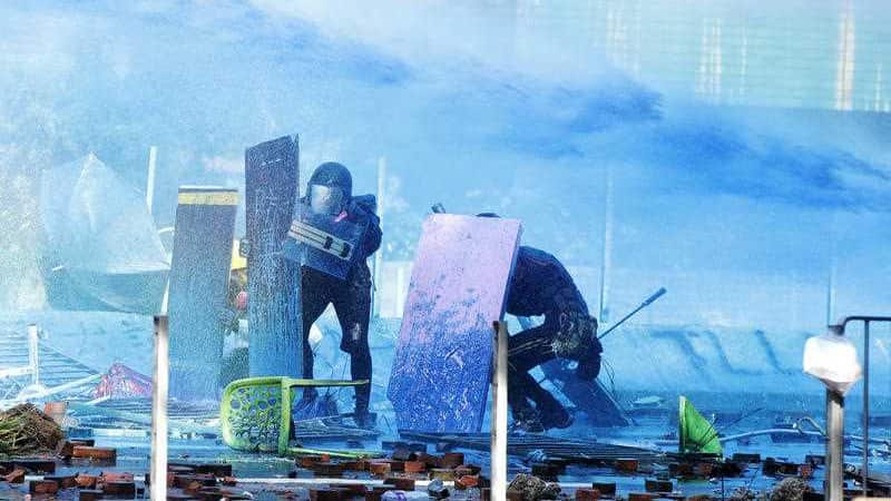 Protestors duck behind shields as a blue-dyed liquid is sprayed from an armored police vehicle at the Hong Kong Polytechnic University.