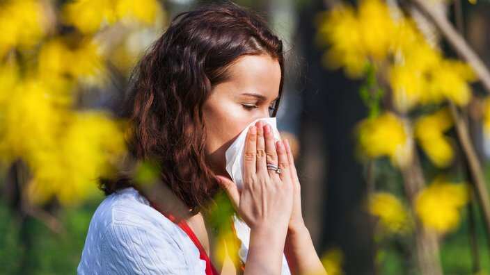 Portrait of a young brunette woman blowing her nose when standing close to flowers in a park