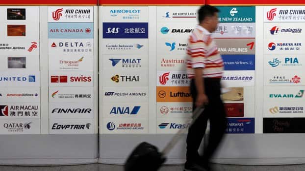 A passenger walks with his luggage past an Air China service information board showing logos of other global airlines at Terminal Three of the Beijing Capital International Airport in Beijing