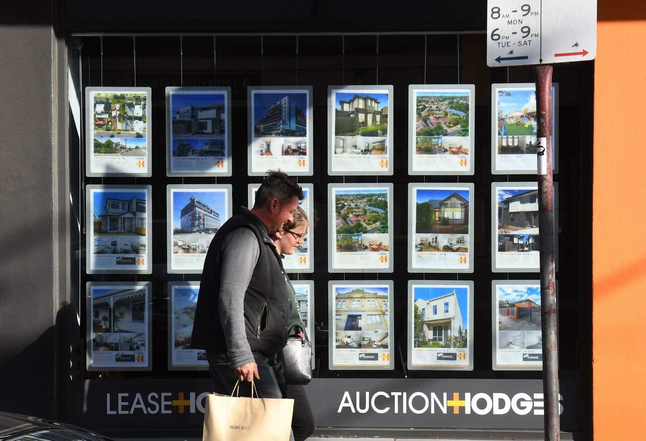 A couple walks past a real estate agent's window advertising houses for sale and auction in Melbourne.