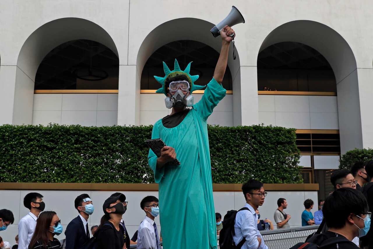 A protester dressed as the Statue of Liberty poses as people march past from Charter Garden to the U.S. Consulate in Hong Kong,