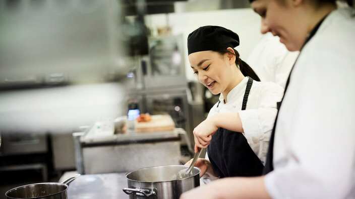 Female chef student with colleague cooking food in commercial kitchen