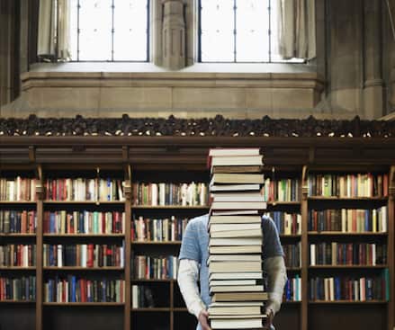 Young man carrying stack of books in university library