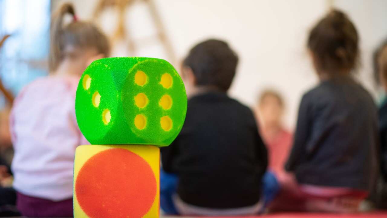Two cubes stand in a day care center in front of children sitting in a circle. 