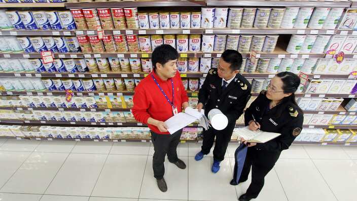 Chinese market inspectors talk with a worker as they inspect baby formula for sale at a supermarket in Hefei city, east China's Anhui province