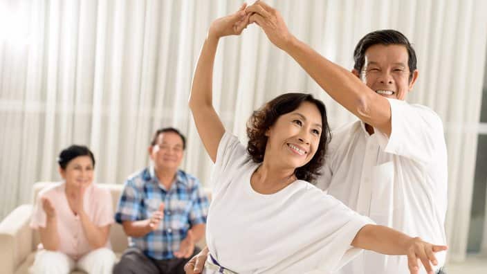 Asian senior couple dancing while their friends are cheering in background