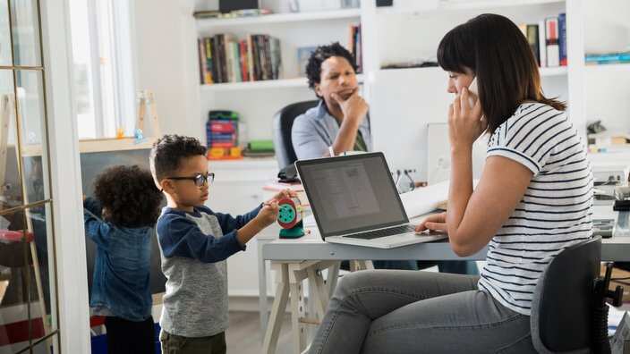 Parents working in home office with children playing