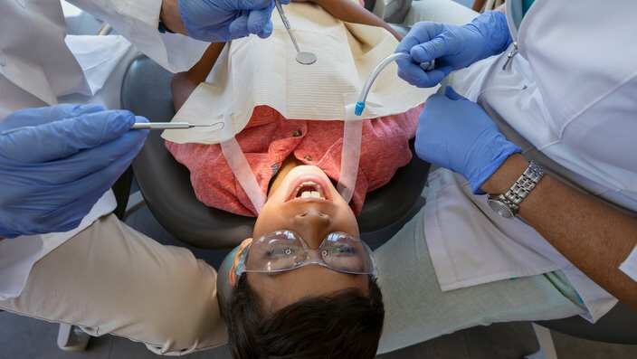 Dentist and dental hygienist checking teeth of boy in dentist office
