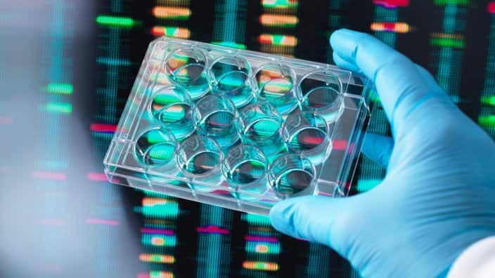 DNA Research, Scientist holding up a multi well plate containing DNA samples with results on the computer screen