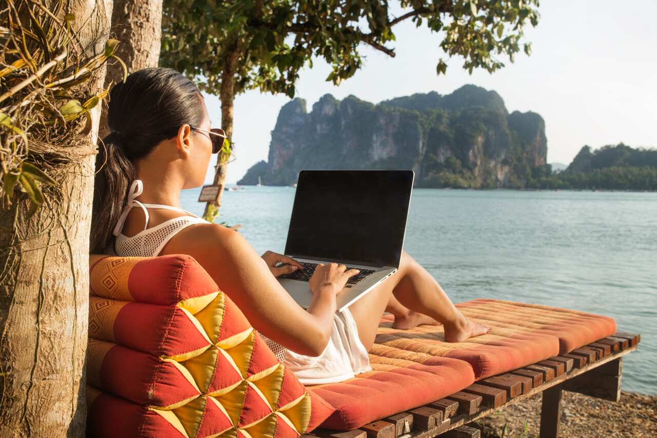 Woman using laptop computer while sitting on lounge chair against sea