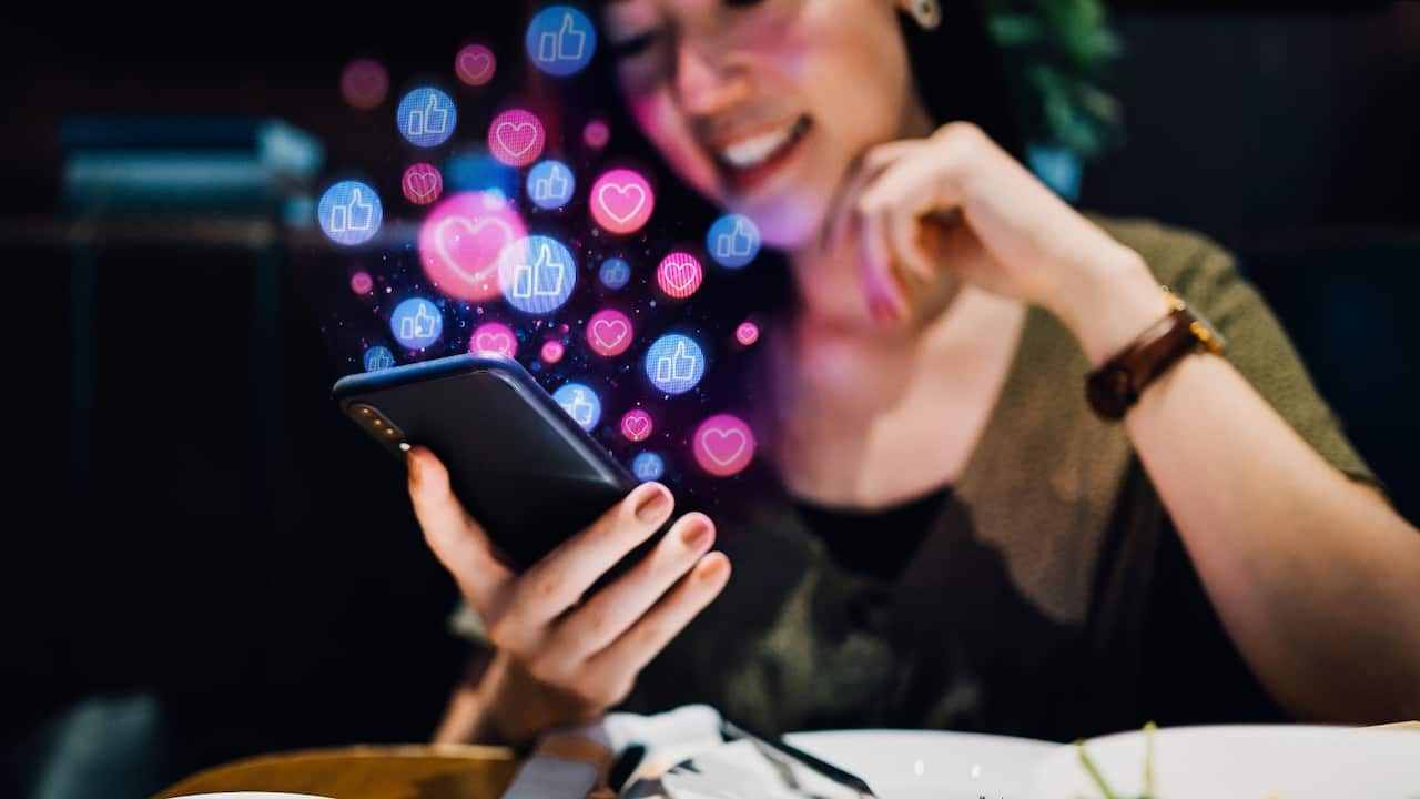 Smiling young Asian woman using smartphone on social media network application while having meal in the restaurant.