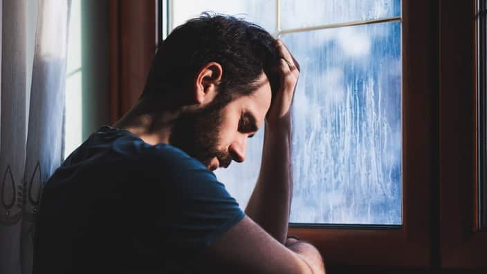 Young sad man sitting by the window.