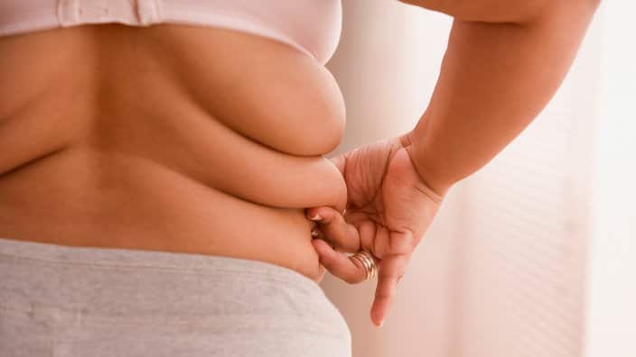 Overweight woman pinching a roll of fat on her side