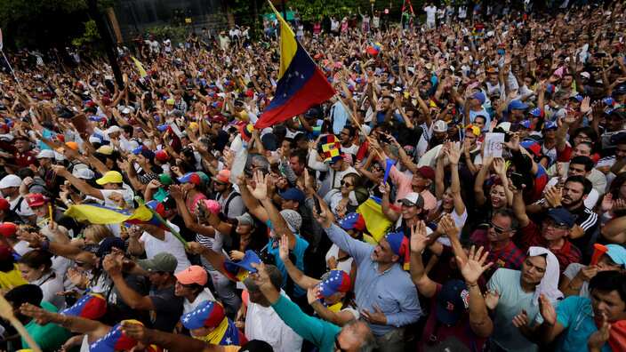 Anti-government protesters hold their hands up during the symbolic swearing-in of Juan Guaido