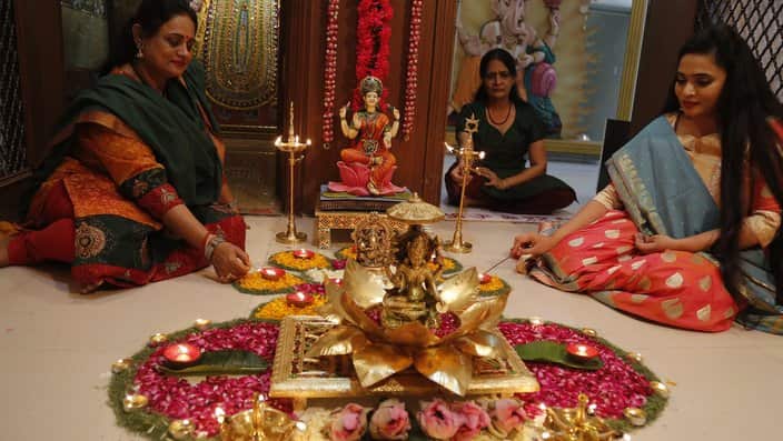 Women light earthen lamps on a Rangoli, as part of Diwali festivities.