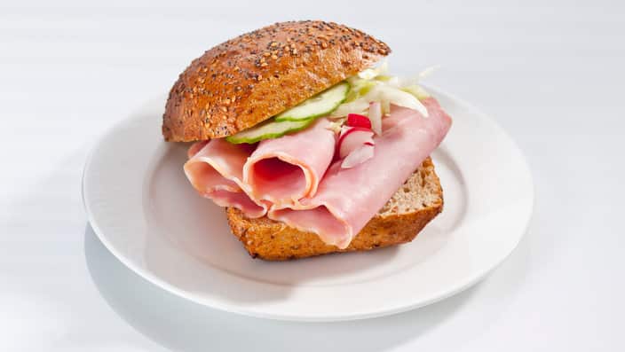 Sandwich of whole grain bread roll with ham on plate