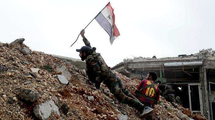 A Syrian army soldier placing a Syrian national flag during a battle with rebel fighters