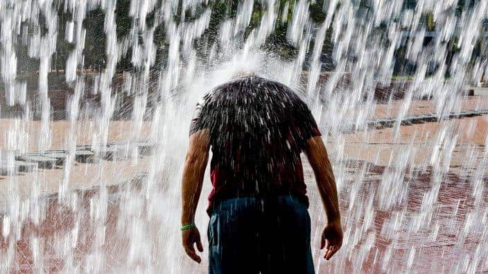 A man standing under falling water during a heat wave