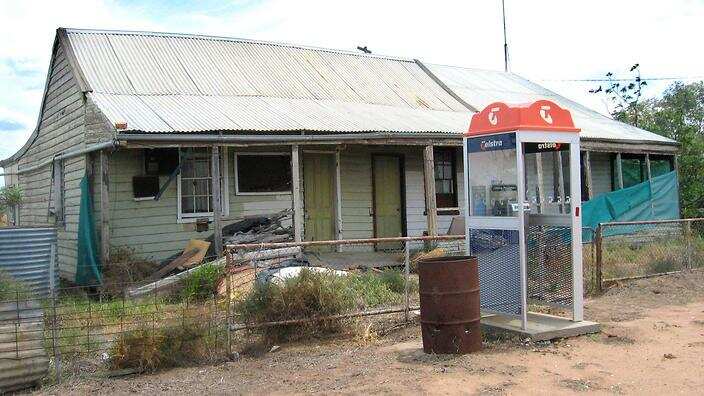 A Telstra payphone sits outside a rundown house
