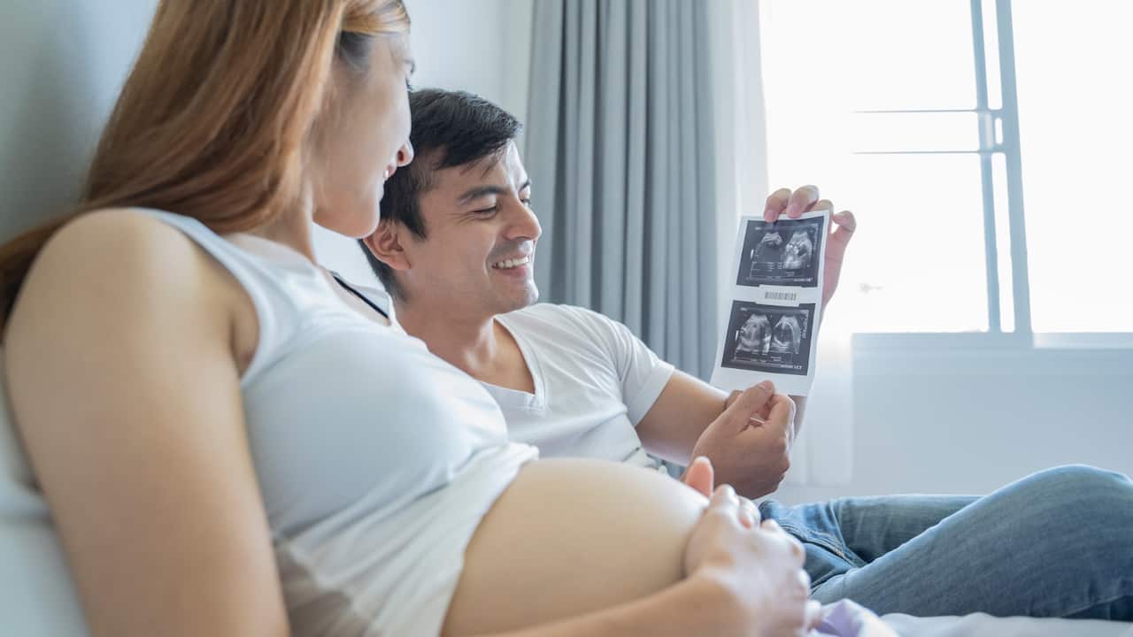 man looking at ultrasound with pregnant woman by his side