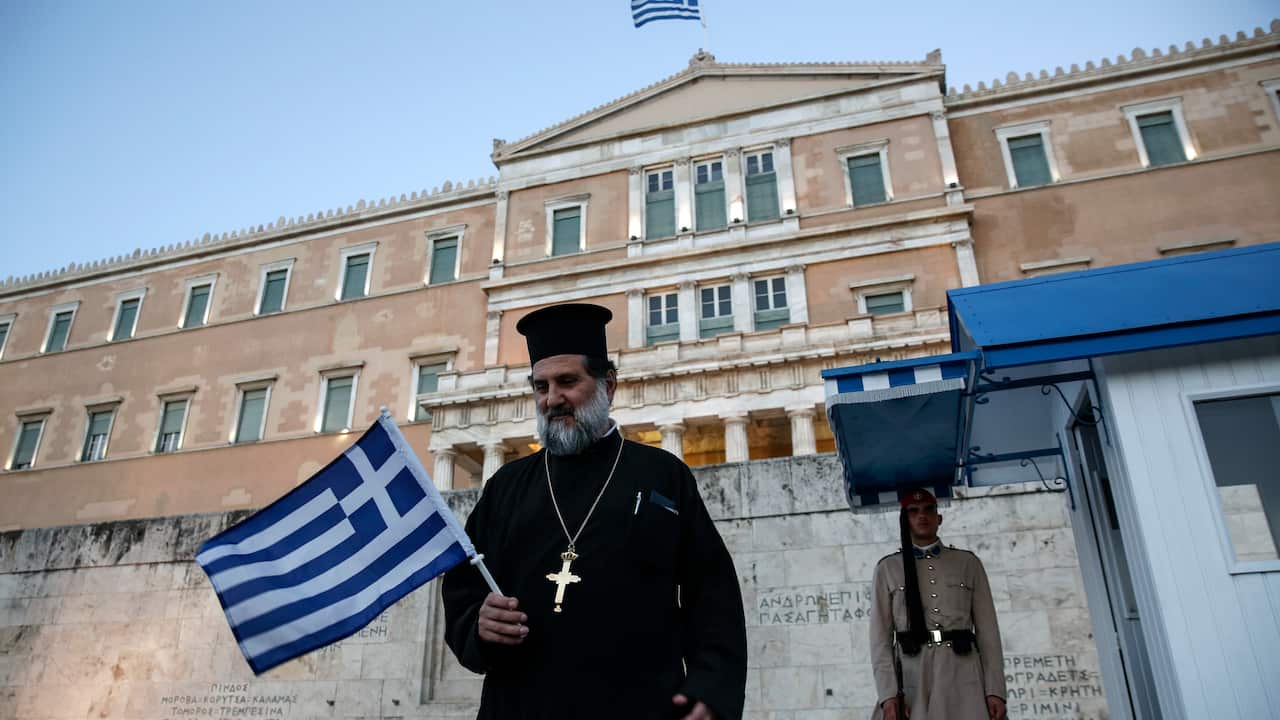 Greek Orthodox priest holding a national flag in front of the Parliament in Athens