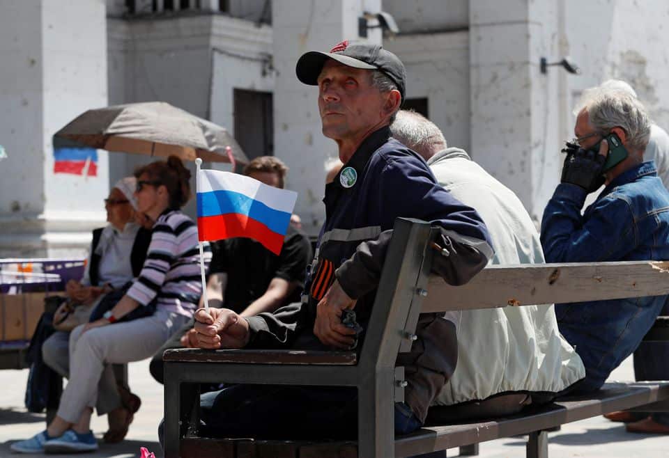 A man holds a Russian flag as he sits in front of a theatre building destroyed during Ukraine-Russia conflict in the southern port city of Mariupol, May 30 2022