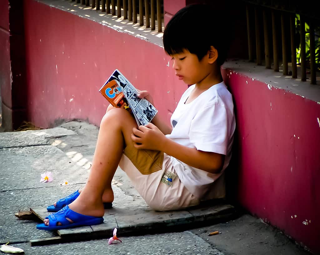 A boy reading a comic book outside the house.