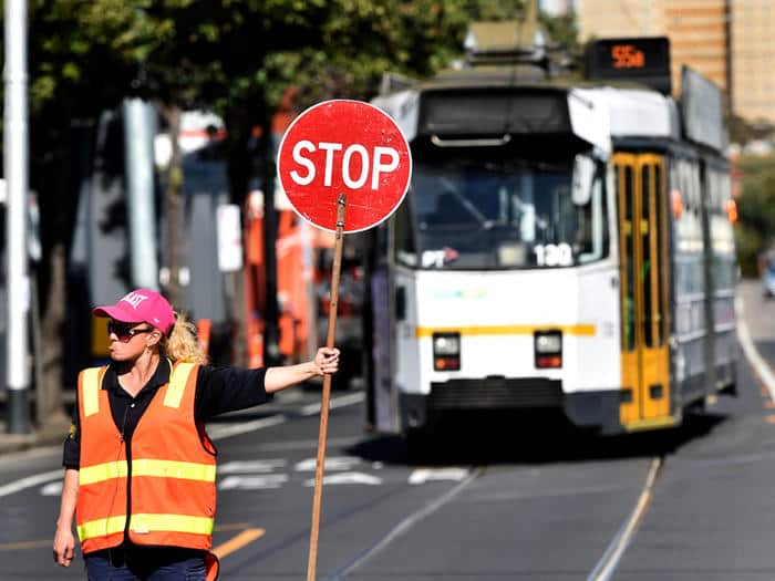 A traffic controller holds a stop signs as a tram rejoins the network on Mount Alexander Road in Melbourne, Thursday, Sept. 10, 2015. Yarra Trams drivers today went on strike over better pay and conditions. (AAP Image/Julian Smith) NO ARCHIVING