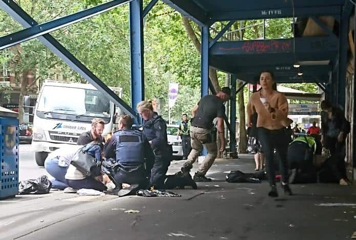 Members of the public watch as police and emergency services attend to an injured person after a car hit pedestrians in central Melbourne, Australia