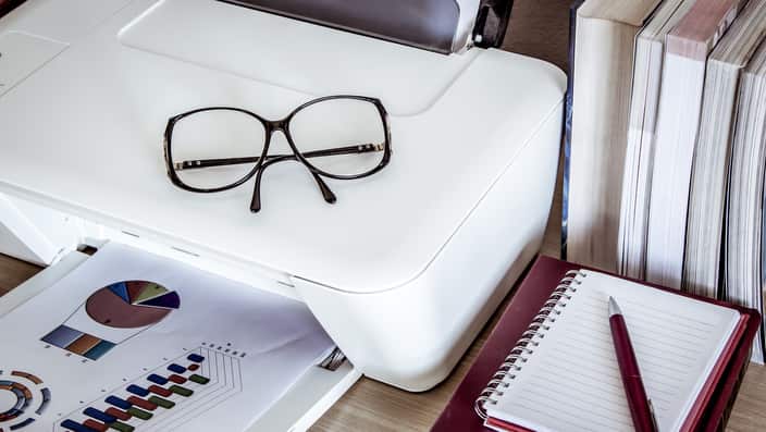 eyeglasses on printer with books on wooden table