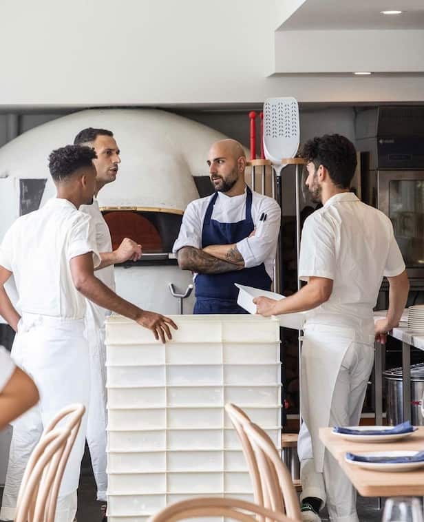 A group of chefs talks in front of a pizza oven