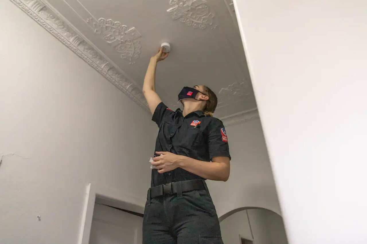 A firefighter checks a smoke alarm. 